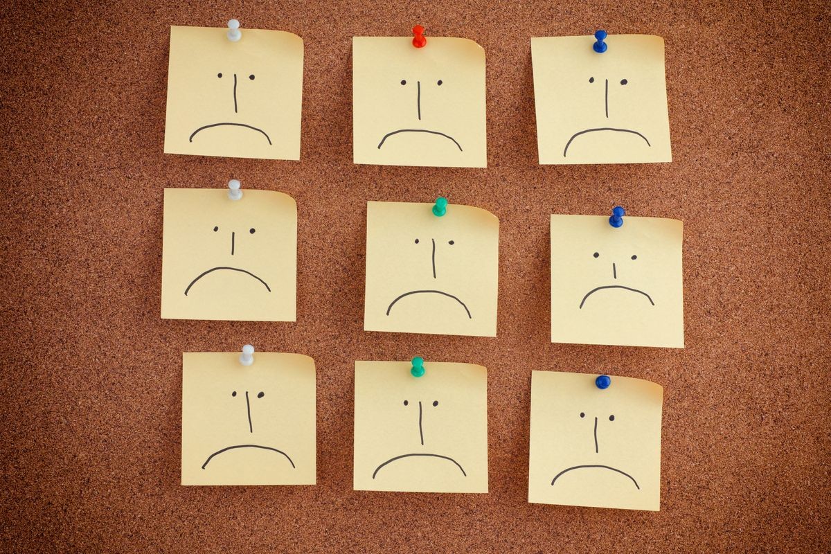 Post it notes with sad faces on bulletin board. Close up.